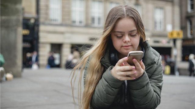 طفلة لديها متلازمة داون تحمل هاتفاً نقّالاً