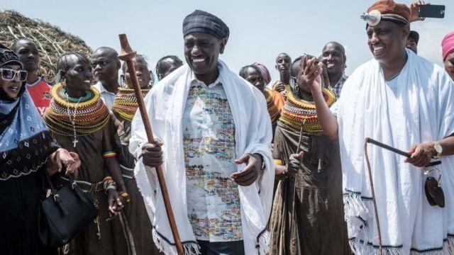 William Ruto (C) and Marsabit County Governor Mohammed Muhamud Ali (R) walk with performers of the Turkana tribe during the 11th Marsabit Lake Turkana Culture Festival in Loiyangalani near Lake Turkana, northern Kenya, on June 28, 2018