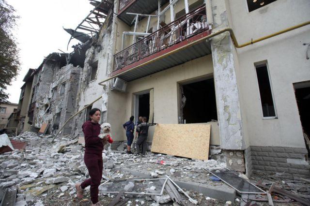 امرأة تحمل كلباً أمام مبنى سكني دمر جزئياً جراء القصف الروسي، خاركيف، شمال شرق أوكرانيا